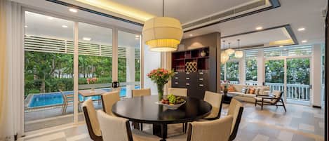A modern dining area with a round table, chairs, a vase with flowers, and a pool view.