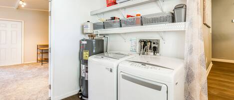 Cocina compacta con refrigerador, lavadora e calentador de agua. Hay un estante pequeño con cestas de almacenamiento y una puerta que da a otra habitación.