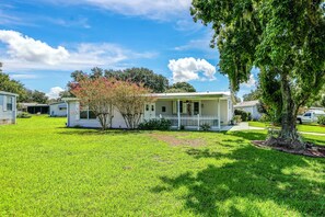 A single-story house with a front porch, surrounded by a well-maintained lawn and a large tree. - Yard & Screened Porch! Villages Escape (Lady Lake)