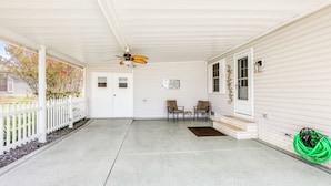 Eine überdachte Veranda mit Deckenventilator, zwei Stühlen, einem kleinen Tisch und einem grünen Gartenschlauch.