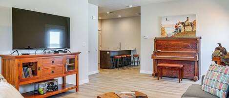 Een woonkamer met een televisie, een houten tv-meubel en een piano.
