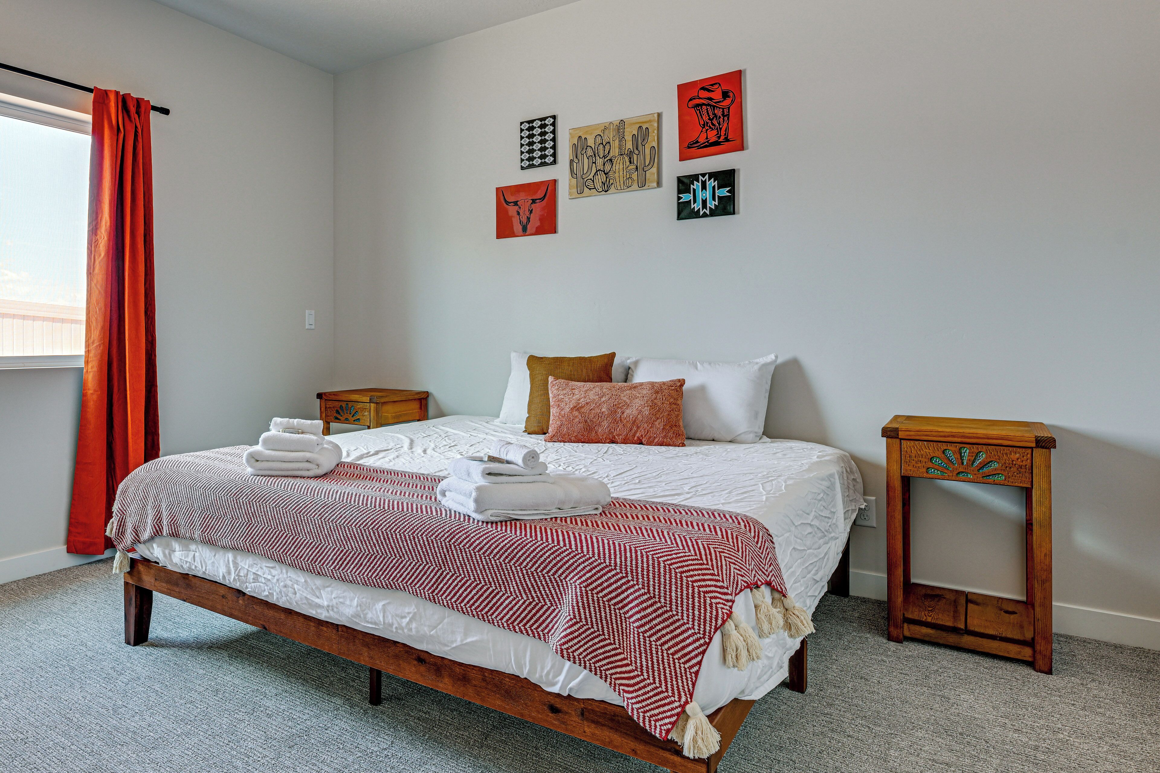 A neatly made bed with a patterned bedspread, a wooden nightstand, a small table, and artwork on the wall.