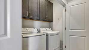 A laundry room with two white front-loading washing machines and a dark wooden cabinet above them. - Explore Glen Canyon/lake Powell! Red River Retreat (Page)