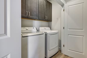 A laundry room with two white front-loading washing machines and a dark wooden cabinet above them. - Explore Glen Canyon/lake Powell! Red River Retreat (Page)