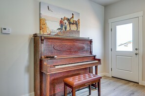 A wooden piano with a bench in front, a painting above it, and a door to the right. - Explore Glen Canyon/lake Powell! Red River Retreat (Page)