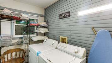 A laundry room with a front-loading washer and dryer, shelves with folded towels, and a sign indicating laundry services.