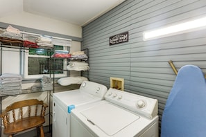 A laundry room with a front-loading washer and dryer, shelves with folded towels, and a sign indicating laundry services.