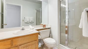 A bathroom with a wooden vanity, a toilet, a glass shower enclosure, and a large mirror with lights above.