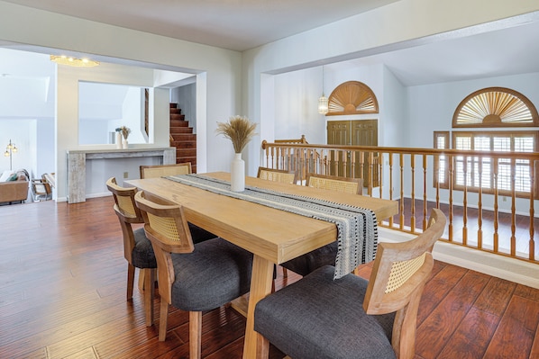 A spacious dining area with a wooden table and chairs, a vase with dried plants, and a staircase with a wooden railing.
