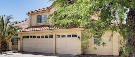A two-story house with a garage, a small window, and a tree in the front yard.
