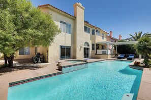 A swimming pool with a tiled edge, a covered patio area, and a building with multiple windows and a chimney.