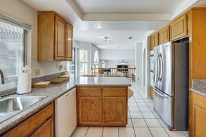 A kitchen with wooden cabinets, a stainless steel refrigerator, granite countertops, and a dishwasher.