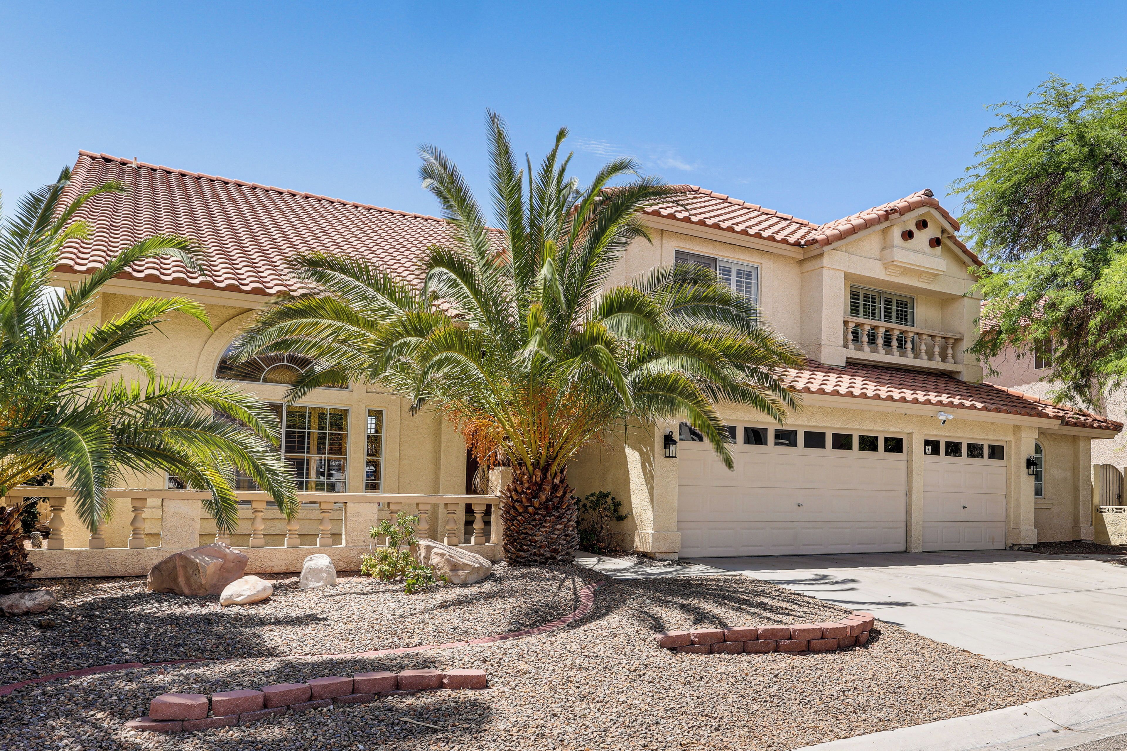 A two-story house with a tiled roof, a garage, and a landscaped front yard with palm trees and rocks.