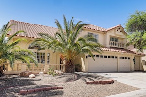 A two-story house with a tiled roof, a garage, and a landscaped front yard with palm trees and rocks.