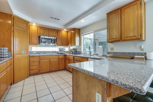 A kitchen with wooden cabinets, a granite countertop, a microwave, and a window with a view.