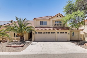 A two-story house with a tiled roof, a garage, and a palm tree in the driveway.