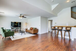 A modern living room with a flat-screen TV, a ceiling fan, and a dining area with bar stools.