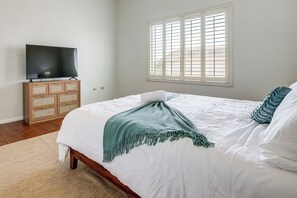 Um quarto com uma cama, uma televisão sobre um móvel de madeira e uma janela com persianas.