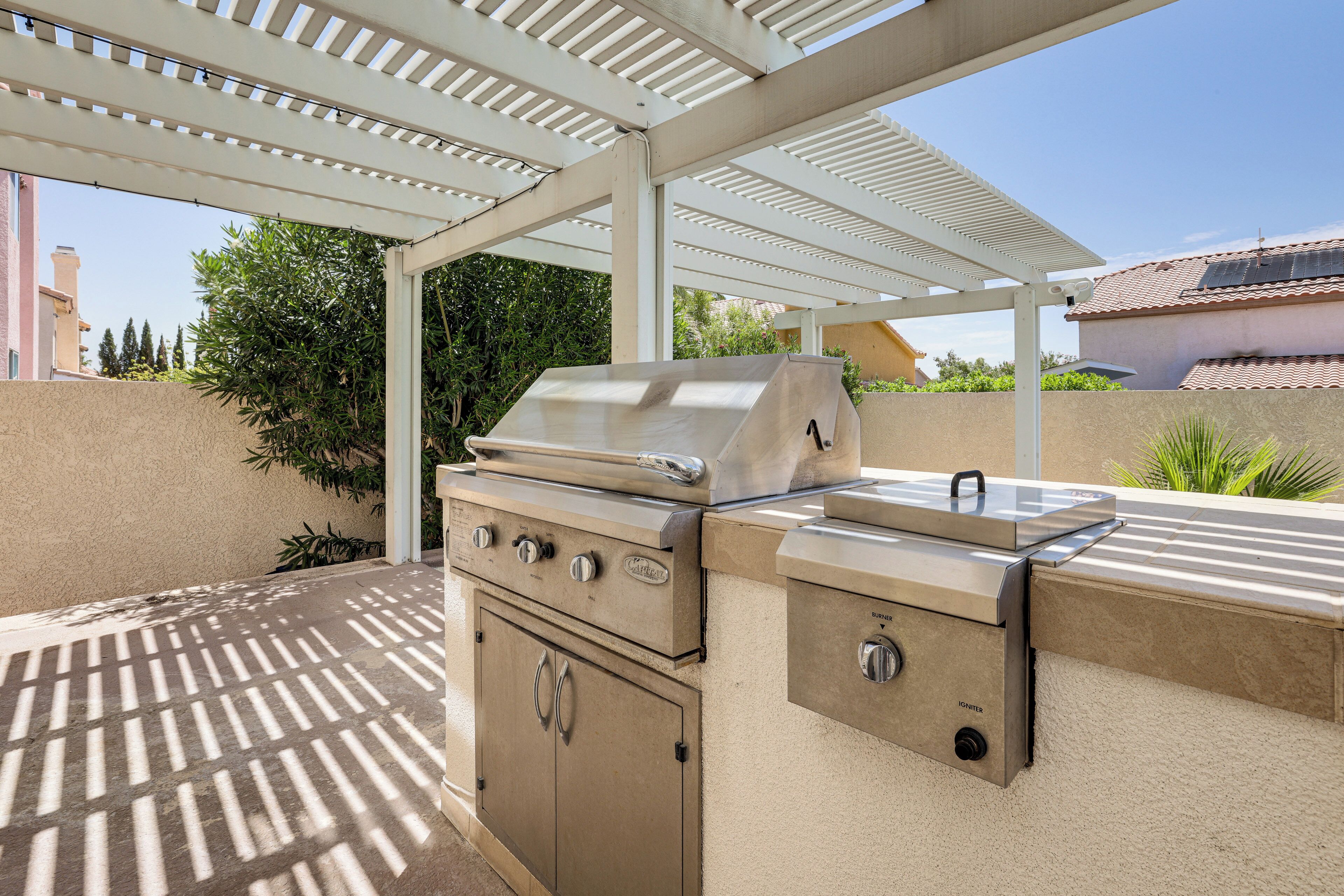 Een buitenbarbecueplaats met een overdekte pergola, een ingebouwde oven en een gasbrander.