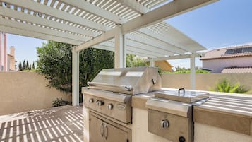 Een buitenbarbecueplaats met een overdekte pergola, een ingebouwde oven en een gasbrander.