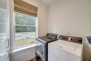 A laundry room with a washing machine and dryer, a window with a view of a garden, and a door with a handle.