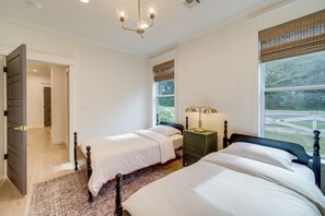 A bedroom with two beds, a chandelier, a nightstand, and a view of the outdoors. - Walkable Rose District Retreat! 15 Mi to Tulsa (Broken Arrow)