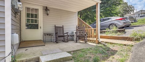 Une véranda couverte avec un banc en bois, une petite table et un marchepied menant à la maison.