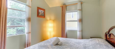 Una cama bien hecha con una colcha estampada, una lámpara de pared y un cuadro en la pared.