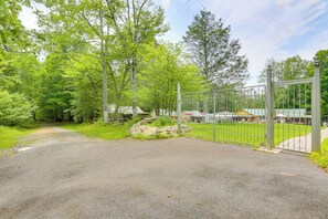 A paved road leading to a gated area with a metal fence, surrounded by lush green trees and a clear sky. - 2-unit Combo, 6 Mi to Bethel Woods Center! (Mongaup Valley)