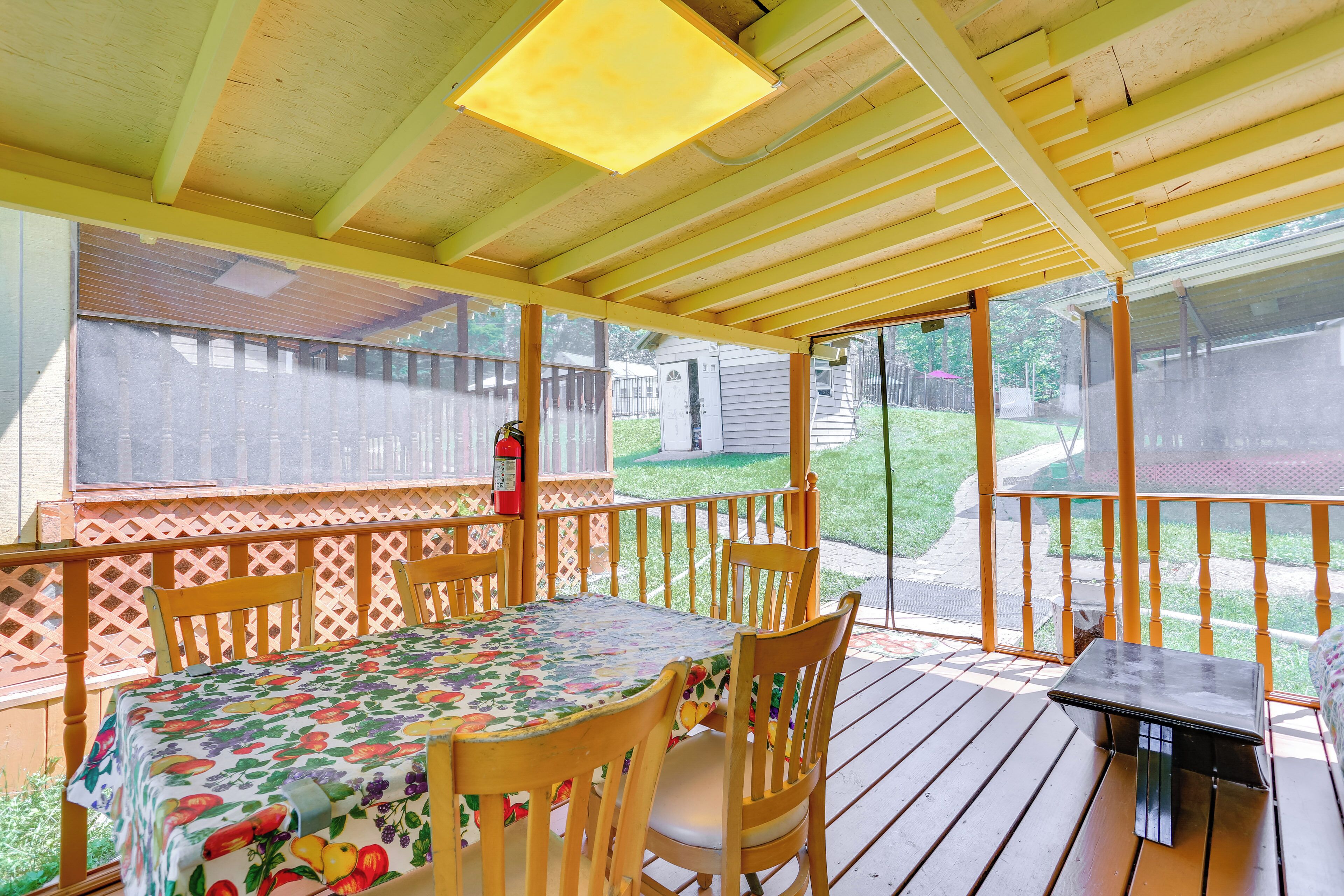 Une terrasse extérieure couverte, équipée d’une table et de chaises, d’une petite table et d’un extincteur.