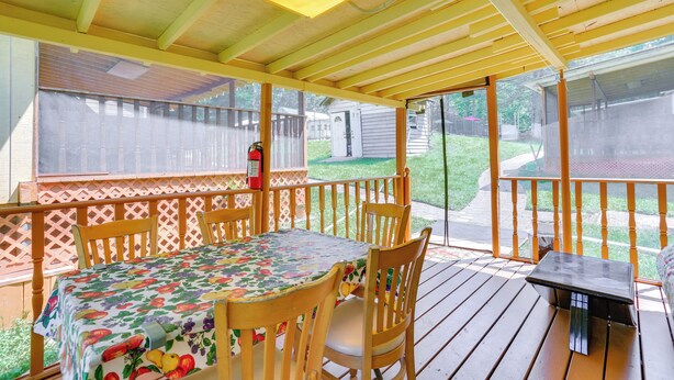 Eine überdachte Terrasse mit Tisch und Stühlen, ein kleiner Tisch und ein Feuerlöscher.