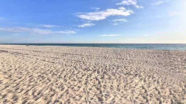 Een breed zandstrand met een helderblauwe lucht en een rustige zee.