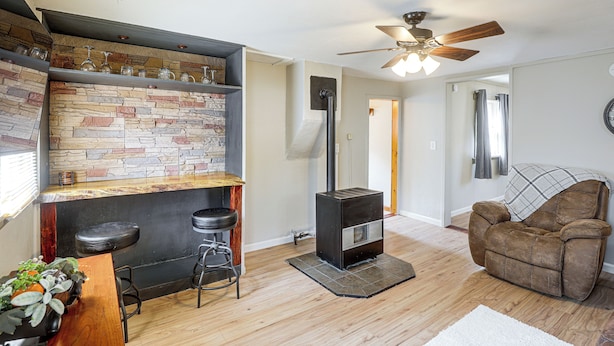A cozy living room with a stone wall, a fireplace, a ceiling fan, and a brown leather sofa. - Walk to Park & Creek! Spearfish Couples Retreat (Spearfish)