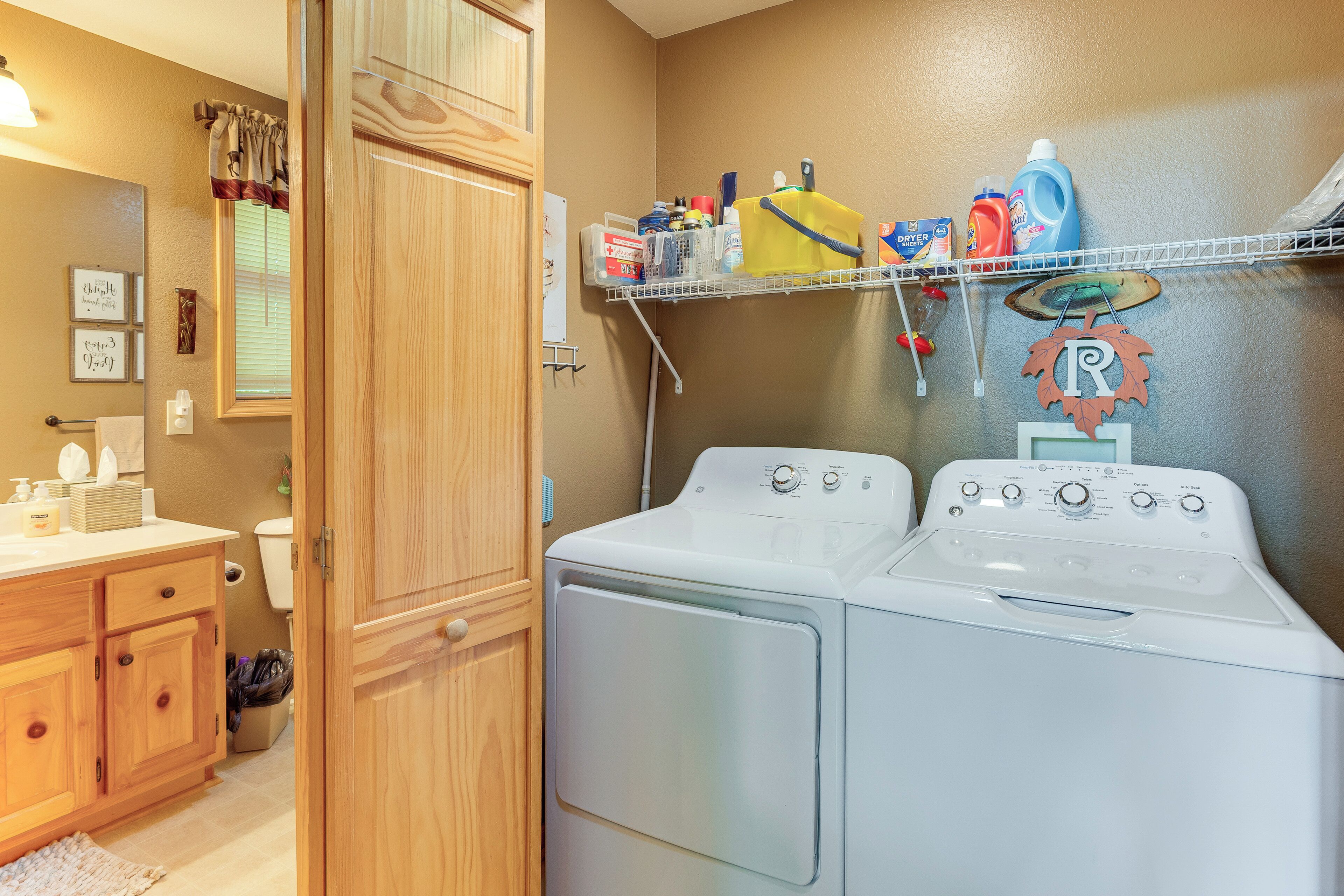 A laundry area with two front-loading washing machines, a wooden cabinet, a shelf with cleaning supplies, and a mirror.