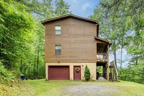 Eine zweistöckige Holzhütte mit Garage, einer Veranda und einer Treppe, die zu einem oberen Stockwerk führt.