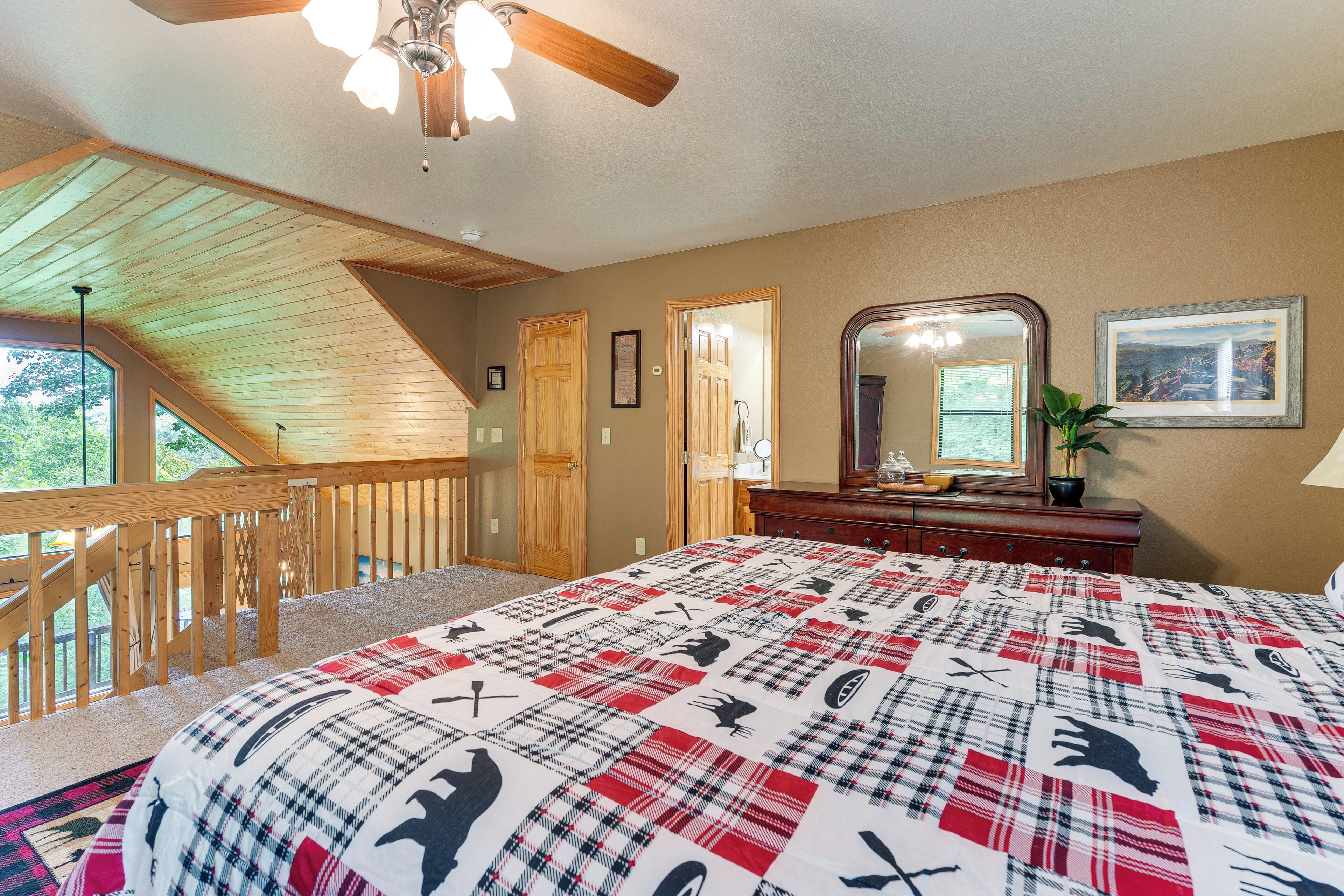 A bedroom with a large bed, a wooden ceiling, a staircase, and a view of the outdoors.