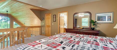 A bedroom with a large bed, a wooden ceiling, a staircase, and a view of the outdoors.