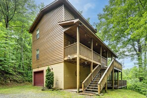 Eine zweigeschossige Holzhütte mit einem Balkon, einer Treppe und einer roten Garagentür.