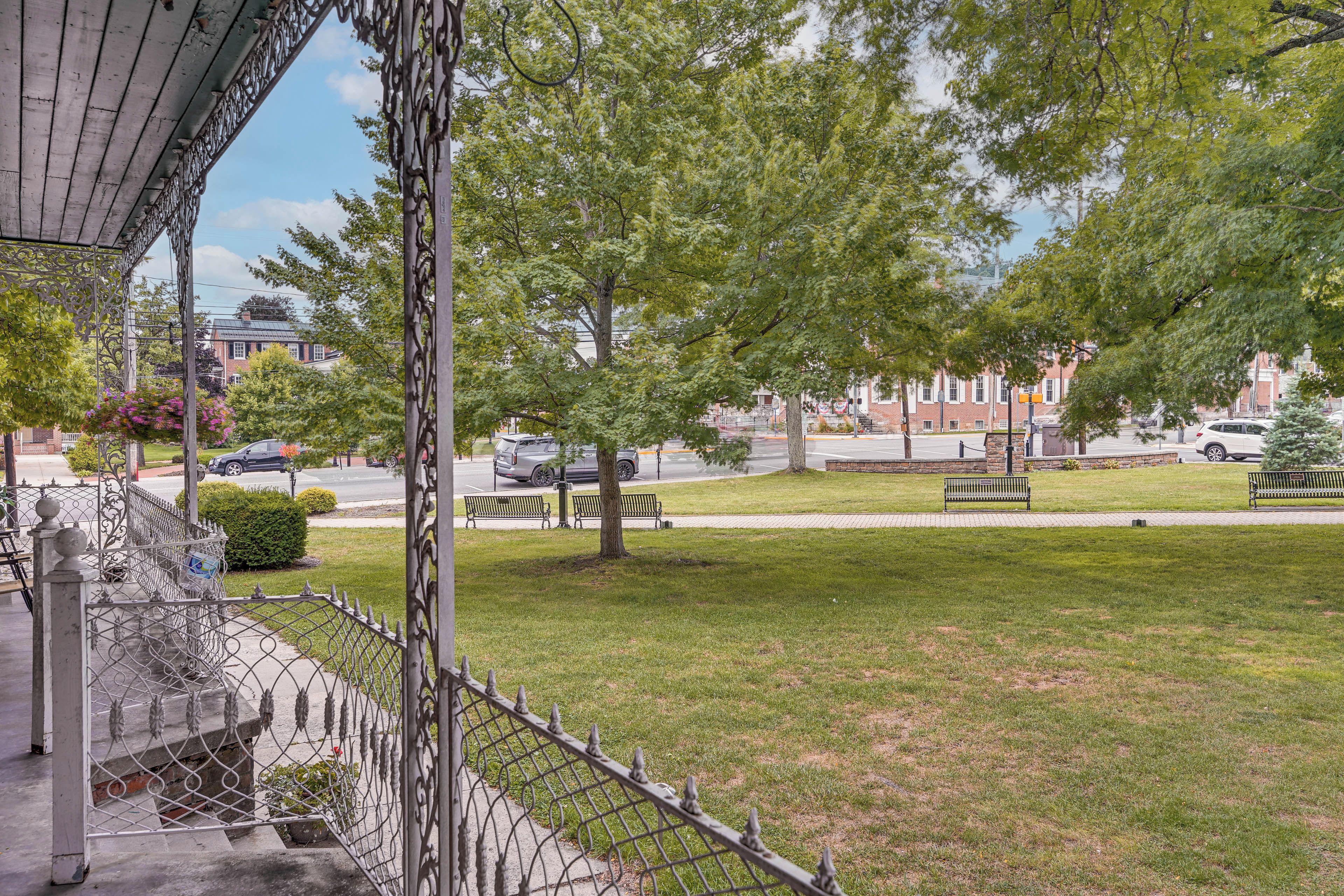 A residential street with a grassy lawn, a metal fence, and a building with a brick facade in the background.