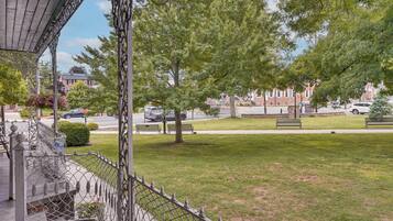 A residential street with a grassy lawn, a metal fence, and a building with a brick facade in the background.