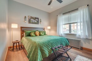 A bedroom with a bed, a radiator, a window with curtains, a standing lamp, and a painting on the wall. - 2-apartment Combo in Dtwn Bedford: Hike & Golf! (Bedford)
