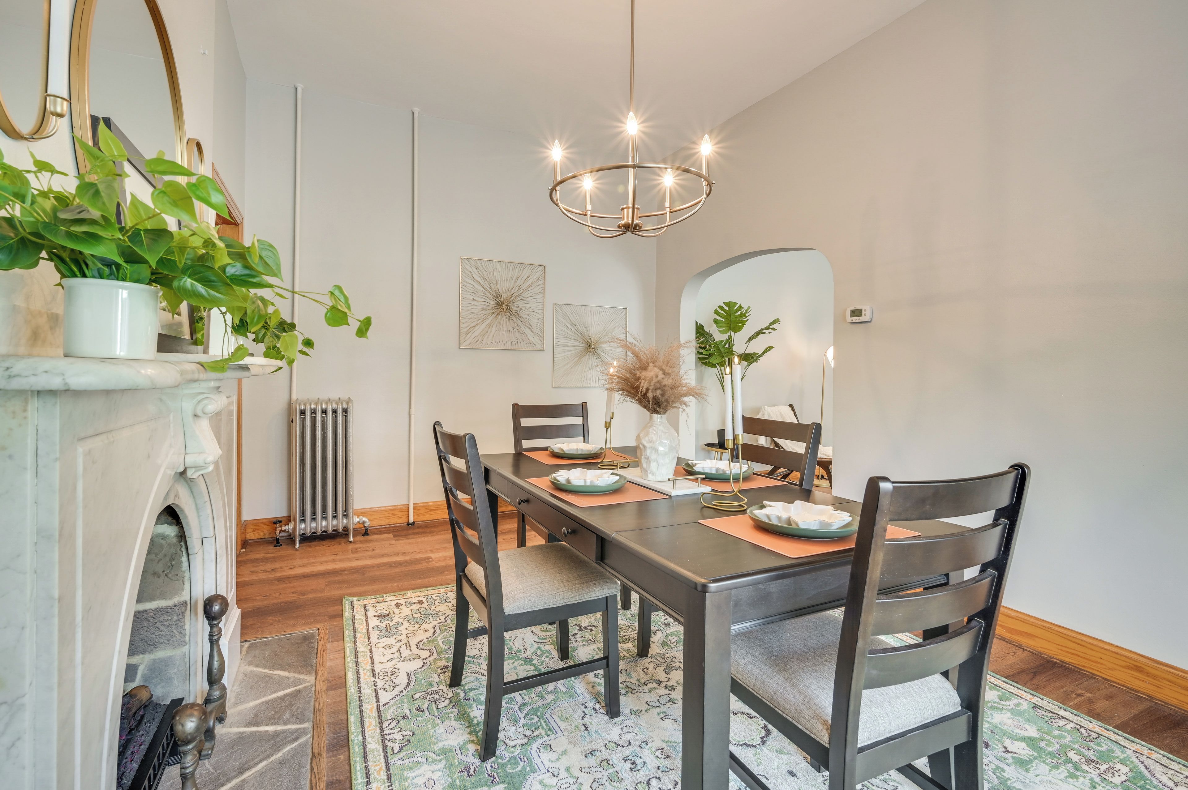 A dining room with a marble fireplace, a chandelier, and a large mirror.