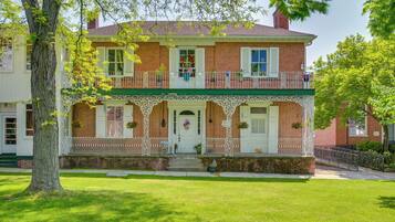 A two-story brick house with a green porch, white railings, and a front door with a wreath.