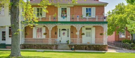 Una casa de ladrillo de dos pisos con un porche verde, barandas blancas y una puerta principal adornada con un adorno festivo.