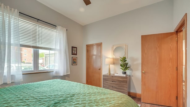 Une chambre avec un couvre-lit matelassé vert, une porte en bois, une commode avec un miroir et une fenêtre ornée de rideaux blancs.