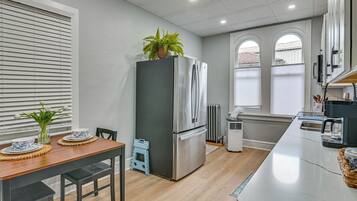 A modern kitchen with a stainless steel refrigerator, a dining table with chairs, and a small plant on top of the fridge.