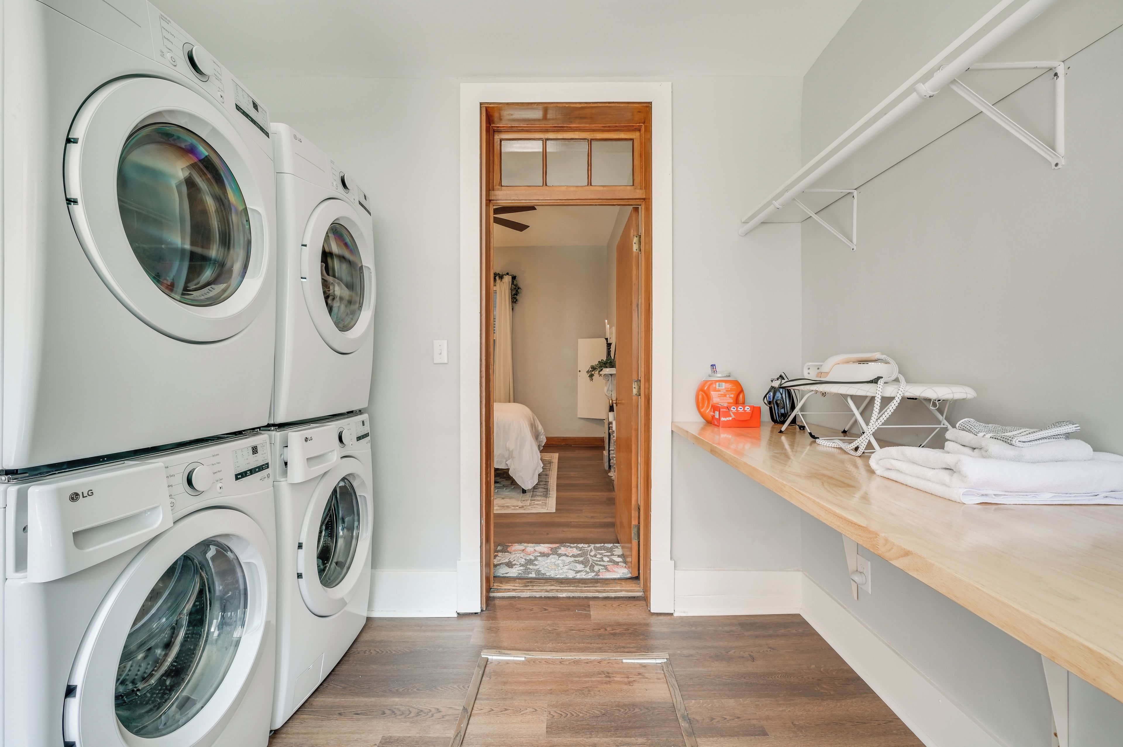 A laundry area with two LG front-loading washers, a wooden door leading to a bedroom, and a wooden countertop with an ironing board and towels.