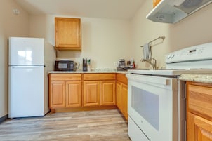 Una cocina con armarios de madera, un refrigerador blanco, un microondas, una estufa y una encimera con varios utensilios de cocina.