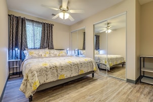 Un dormitorio con cama, ventilador de techo, espejo y ventana con cortinas.