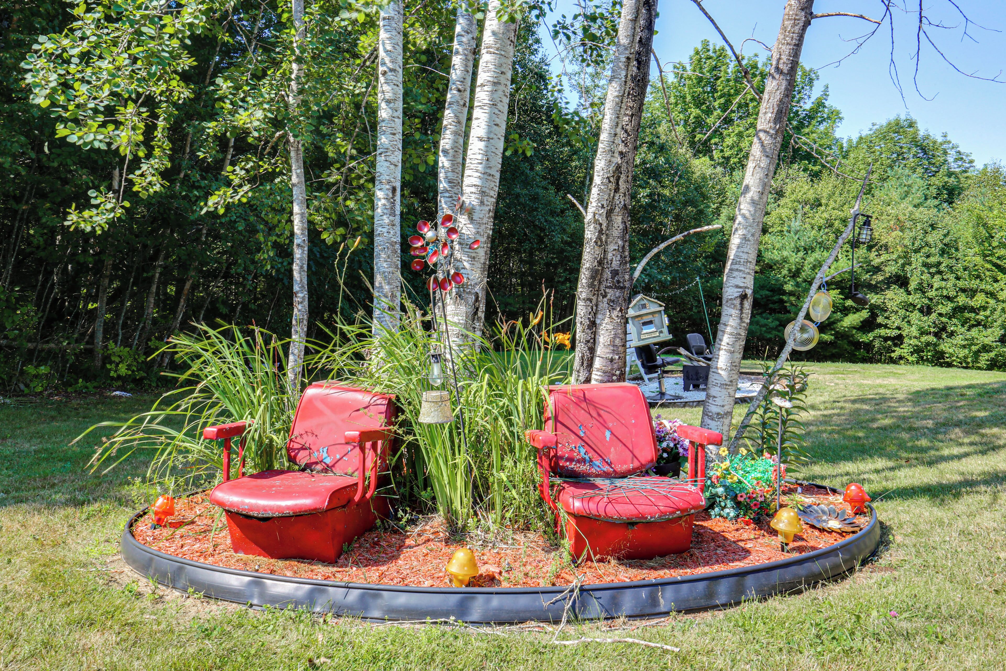 Two red chairs with a small garden area in between, surrounded by trees and a lawn.